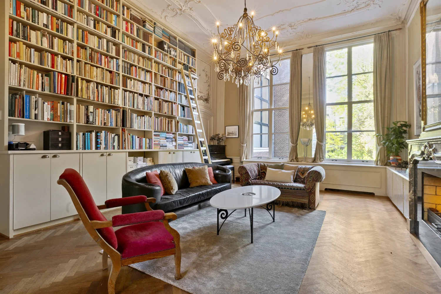 Weelderige woonkamer met boekenwand, kroonluchter en hoge ramen — Keizersgracht Amsterdam